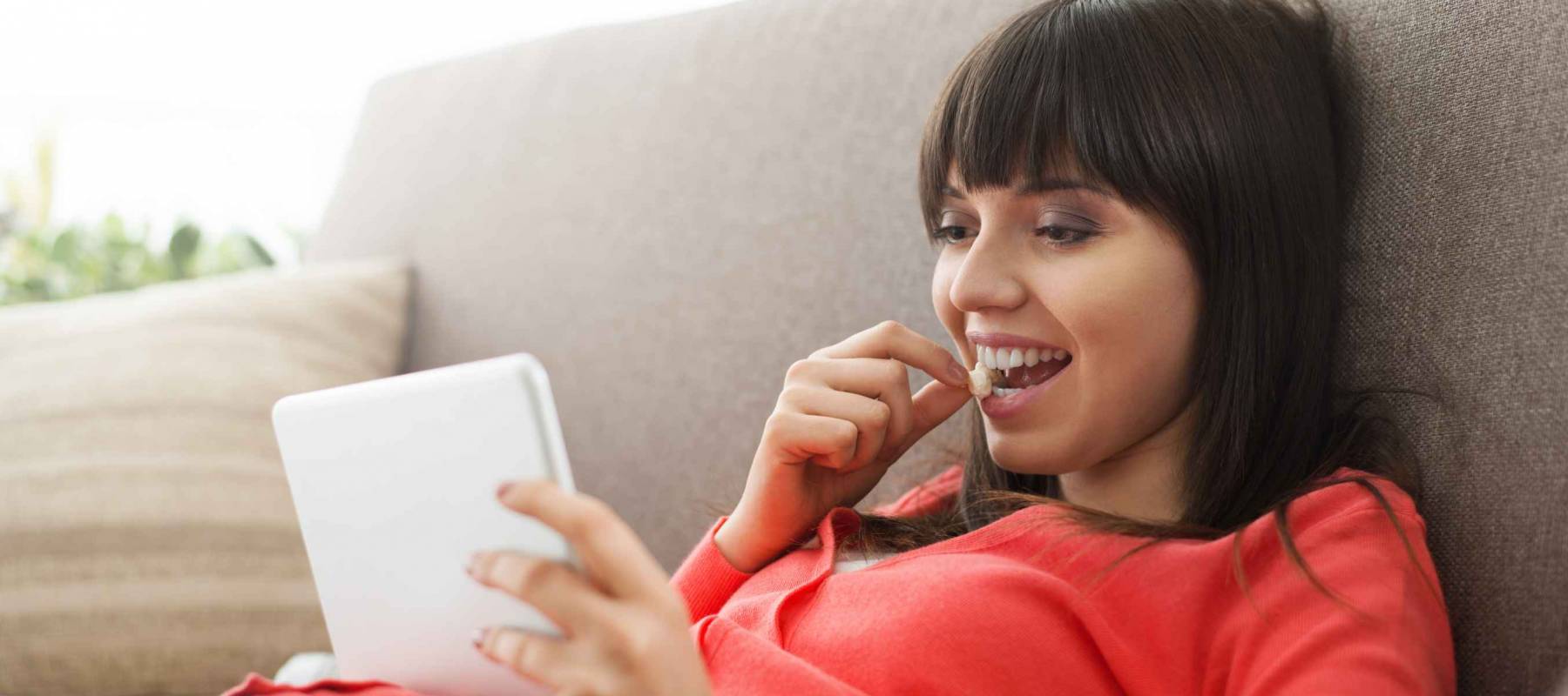 Attractive woman relaxing on the couch at home, she is watching videos online and eating popcorn, movies streaming concept