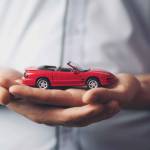 A hand signing a document next to a car key laying on a table