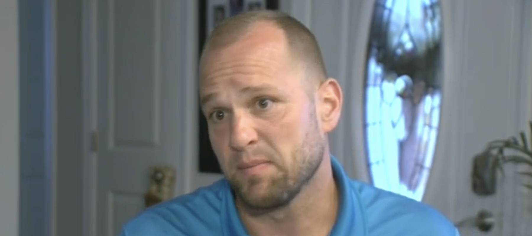 Man sits in dining room, looking at camera, distressed.