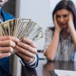 Man holding a fan of cash while wife sits in background