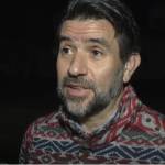 Man speaking to camera, outside, looking serious.