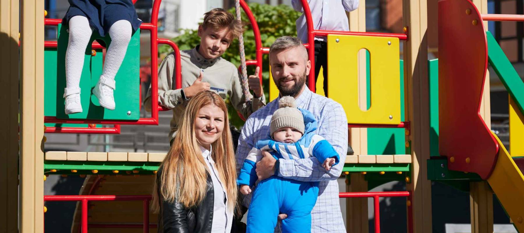 Happy family - father, mother and children having fun together on playground. Three cheerful kids playing while parents holding toddler in arms.