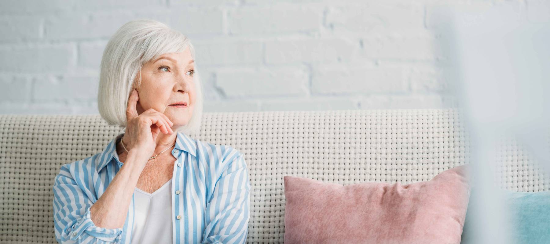 portrait of pensive grey hair woman looking away resting on sofa at home