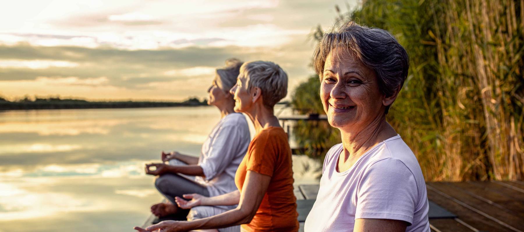 group of Caucasian senior woman doing yoga exercises by the lake