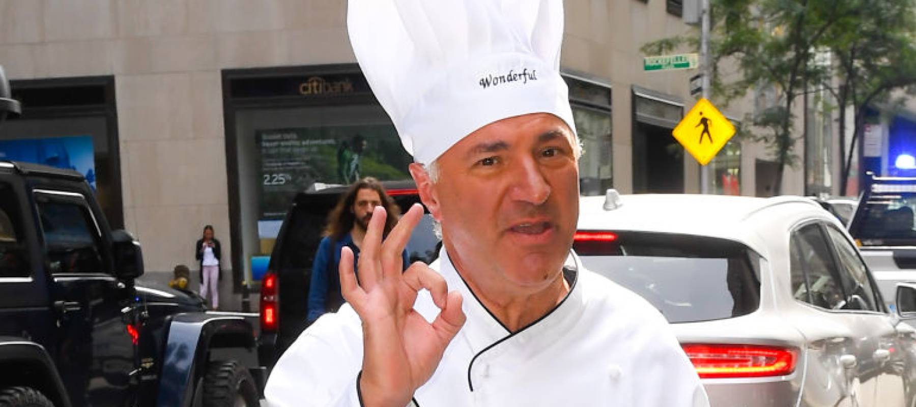 Kevin O'Leary crosses the street in New York, wearing a chef coat and hat.