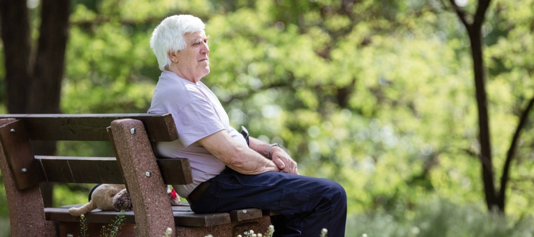 Pensive senior man sitting on bench in summer park