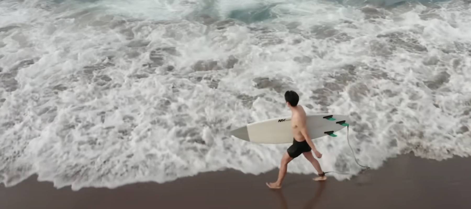 Man walks along the beach with a surfboard under his arm.