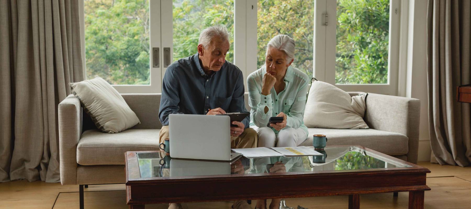 Front view of active senior Caucasian couple calculating bills in living room at home