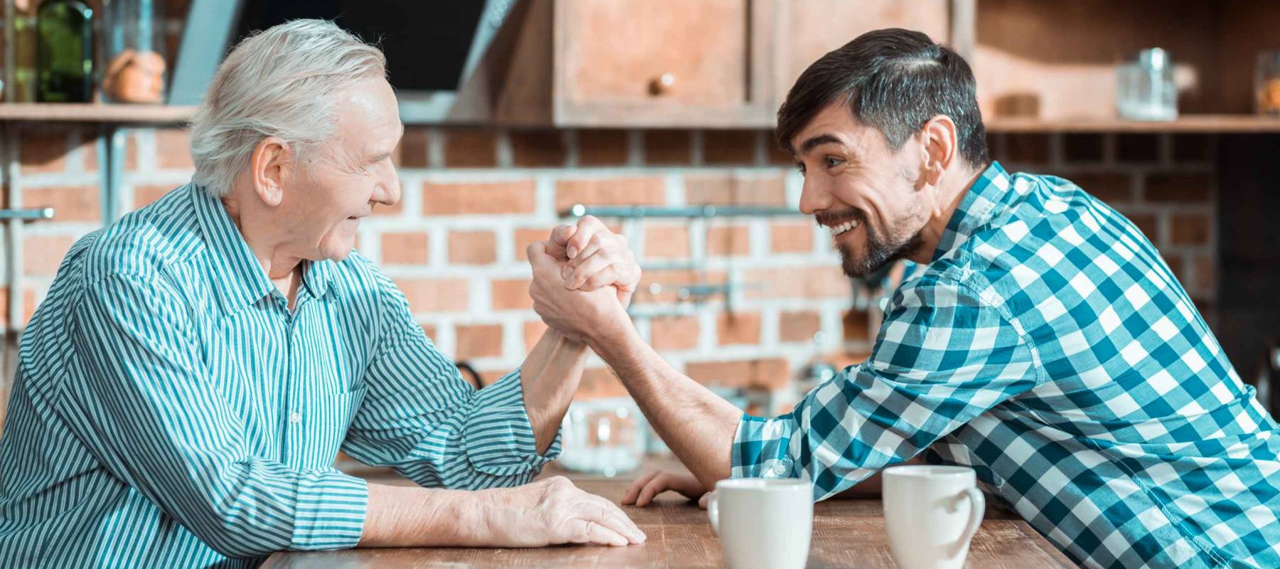 Who is stronger. Nice happy positive father and son sitting opposite each other and playing arm wrestling while deciding who is stronger