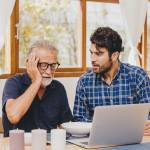 Senior man with adult son looking worried at a computer