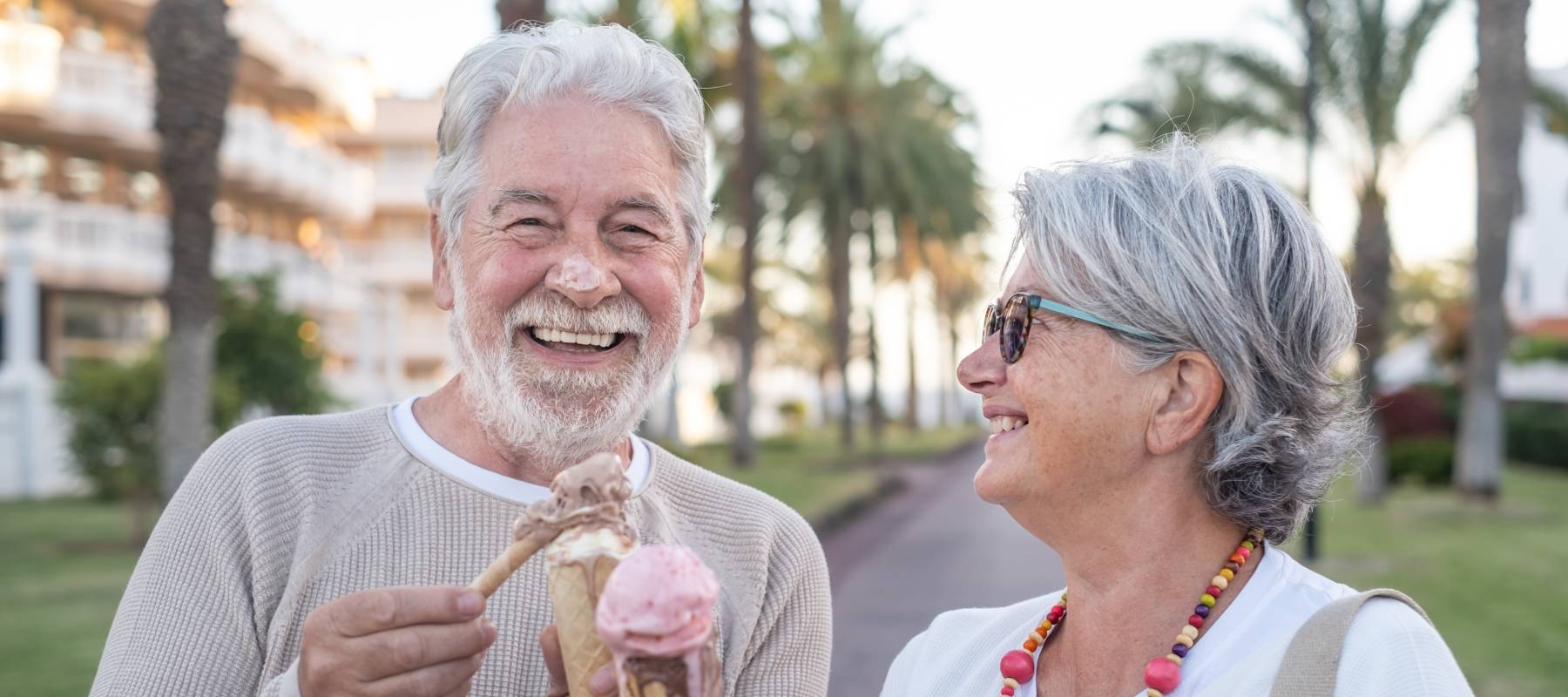 Cheerful senior couple eating ice cream cone in the park laughing.