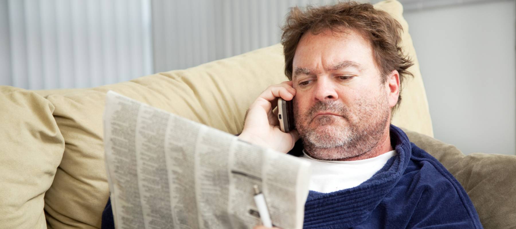 Unemployed man at home on the couch looking at the classified ads in the newspaper.