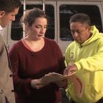 Couple standing outside on driveway, showing reporter something on piece of paper.