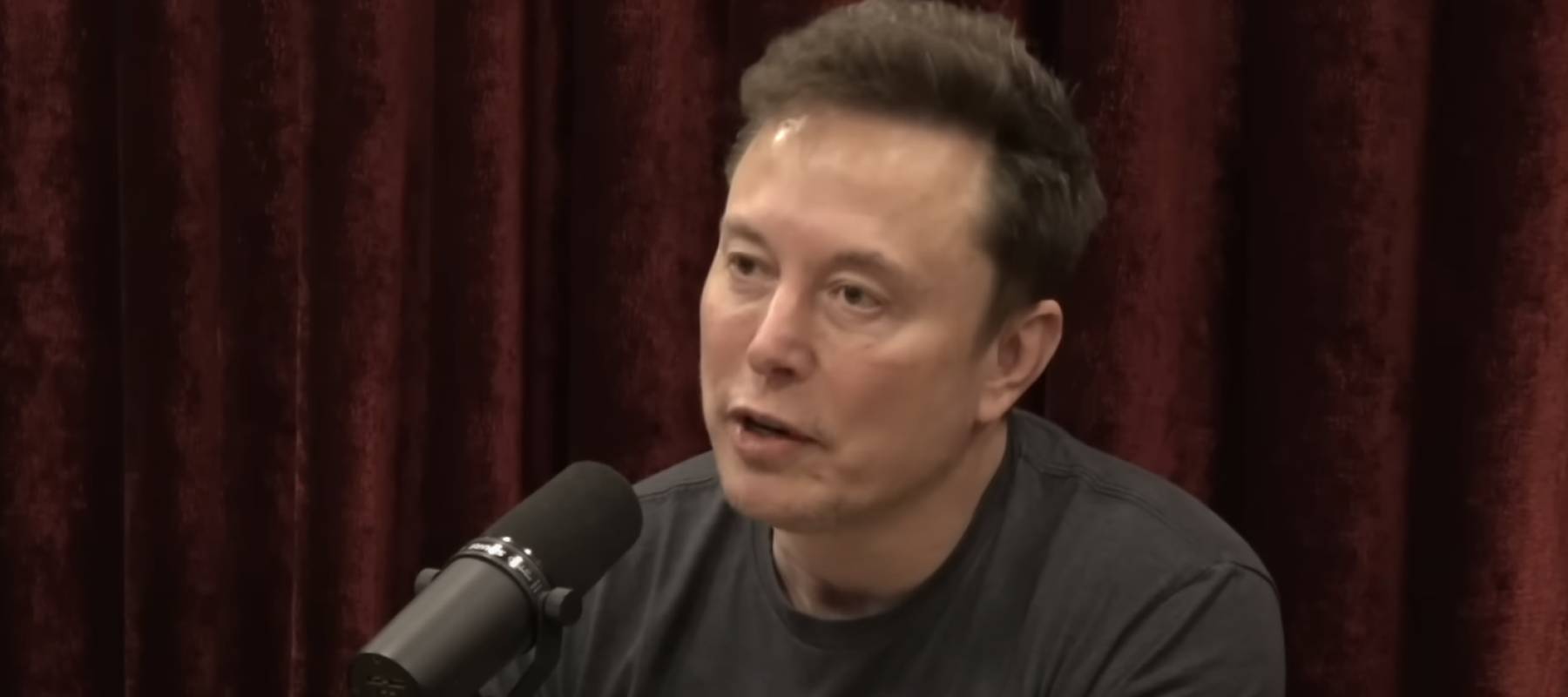 Elon Musk seen on set of podcast, talking into microphone.