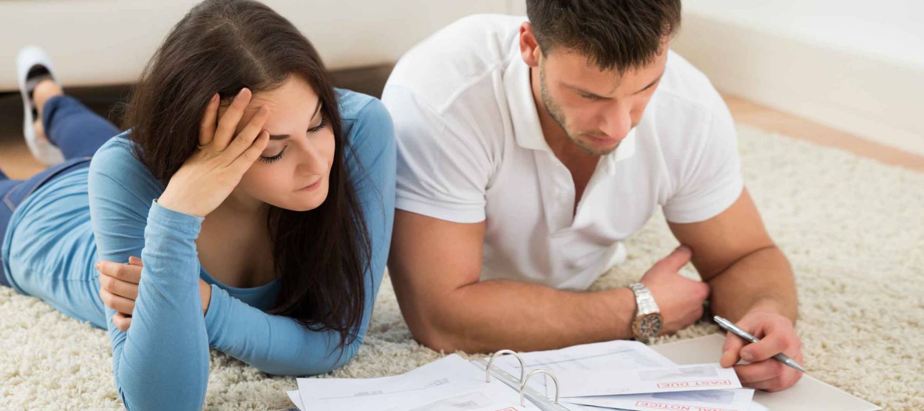 Worried Young Couple Lying On Carpet Calculating Their Bills At Home