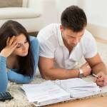Worried Young Couple Lying On Carpet Calculating Their Bills At Home