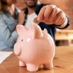 money, home, finance and relationships concept - close up of couple with piggy bank sitting on sofa