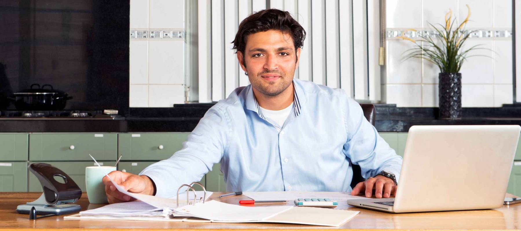 Handsome man doing his personal administration, such as taxes, paying bills and checking his finances at a kitchen table