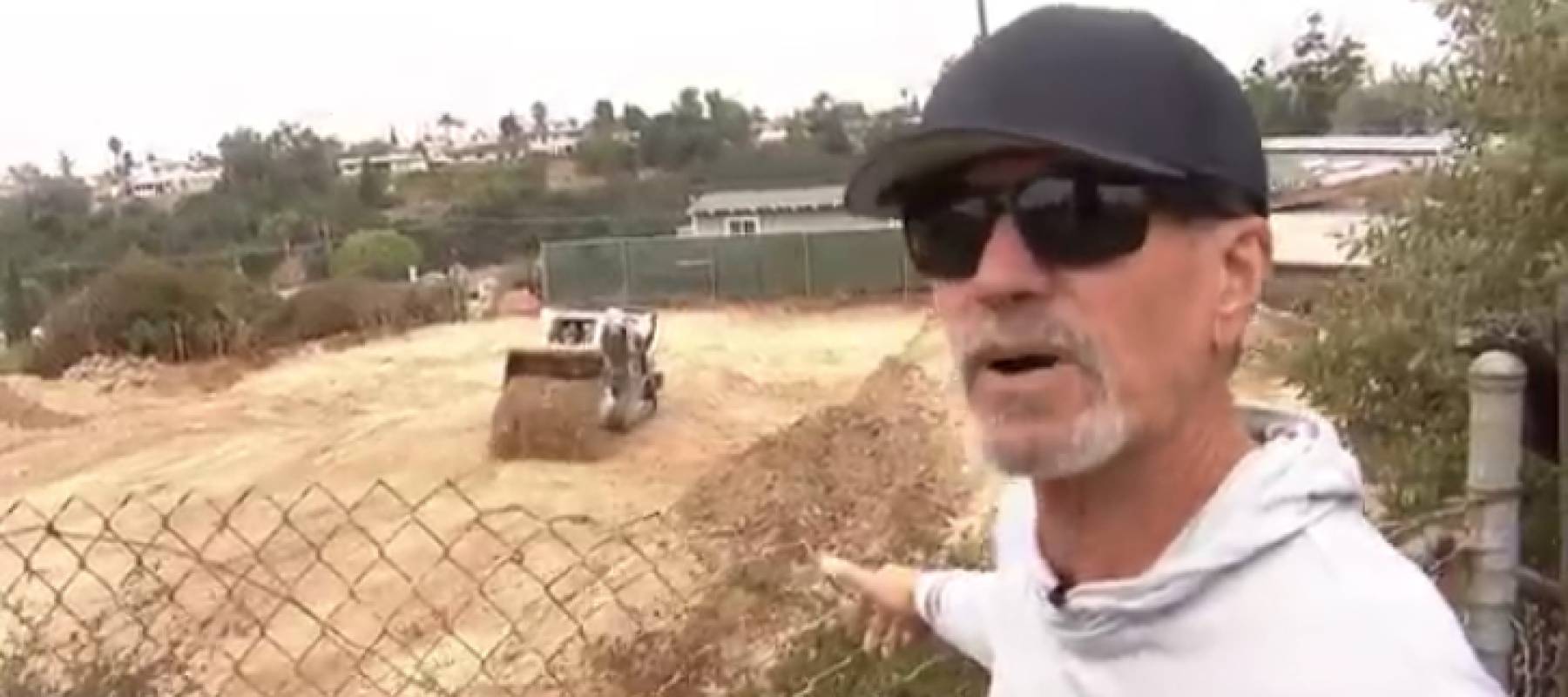 Man in sunglasses gestures angrily at construction site behind him.