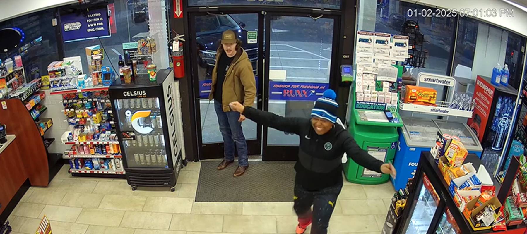 Still of gas station security camera footage, woman in winter hat with arms wide open, smiling.