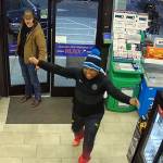 Still of gas station security camera footage, woman in winter hat with arms wide open, smiling.
