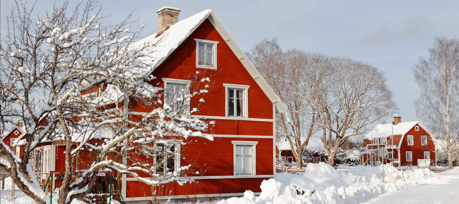 Swedish red two storeywooden  family houses behind a snow covered tree alongside the snow surfaced road in the residential area during the winter season.