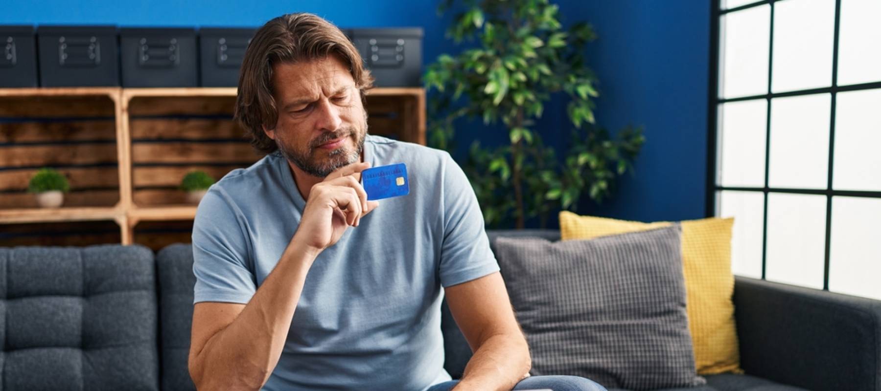 Middle age man using laptop and credit card with doubt expression at home