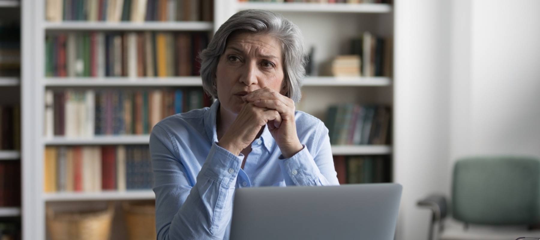 A woman looks away from her laptop pensively.