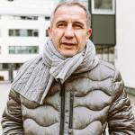 Man bundled up in winter clothing, seen outside, looking dismayed with hands in pockets.