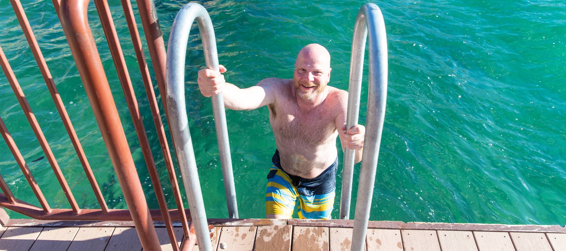 Man climbing out of the water on ladder attached to dock.