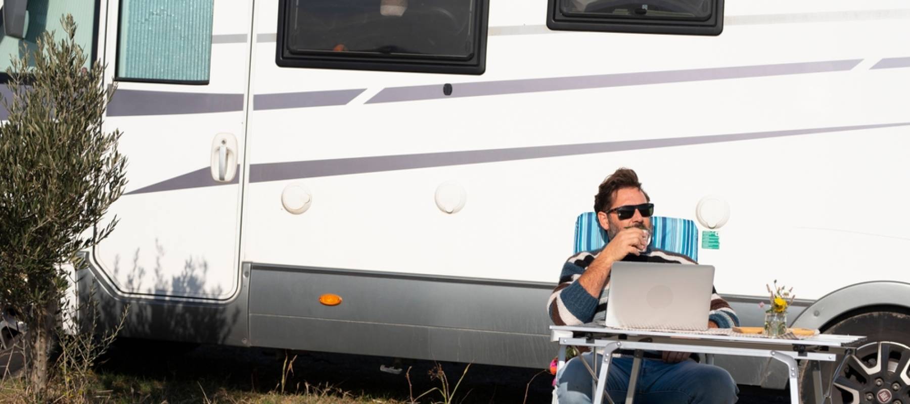A man sits in front of an RV with a laptop on a folding table.