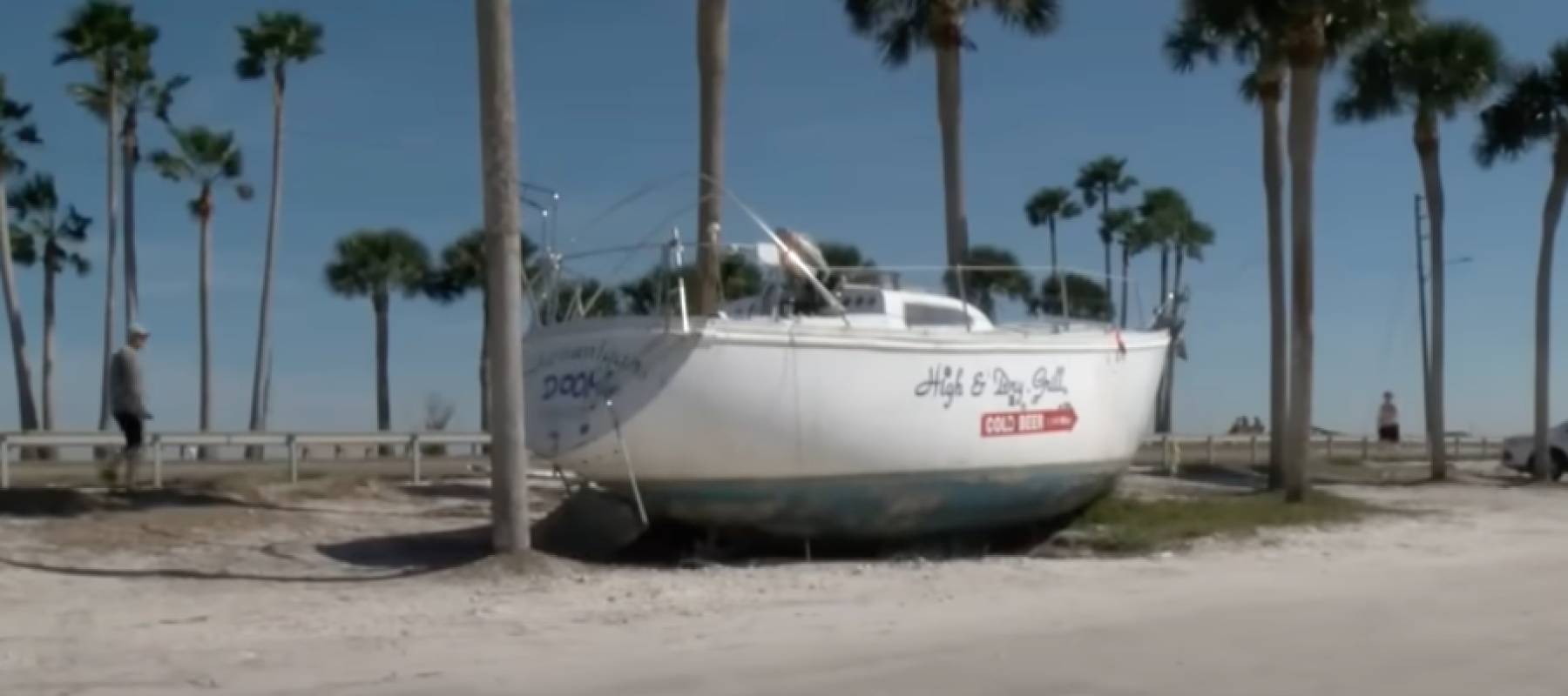 A sailboat sits on shore along a highway.