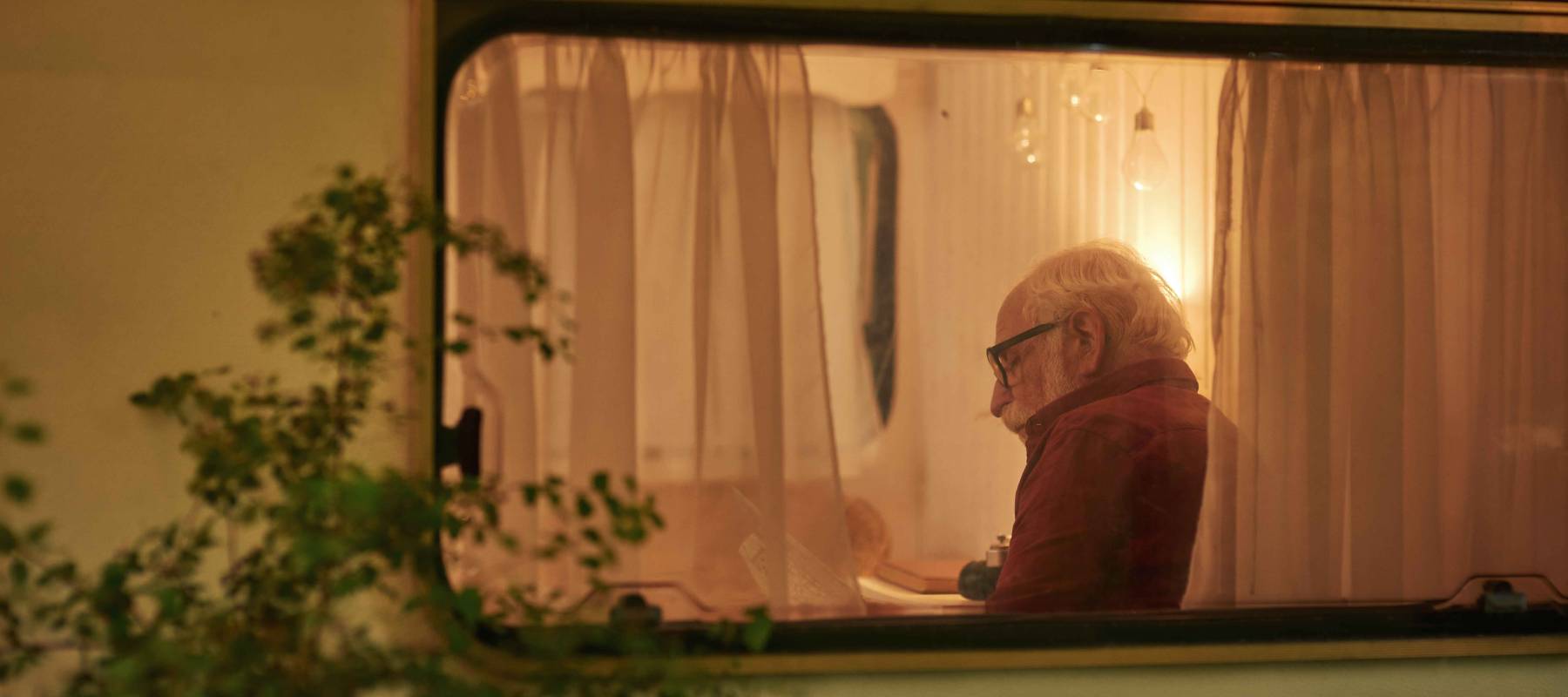 Senior male with map sitting in his camper van in the evening, seen from outside.