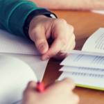 close up of students hands with books or textbooks writing to notebooks