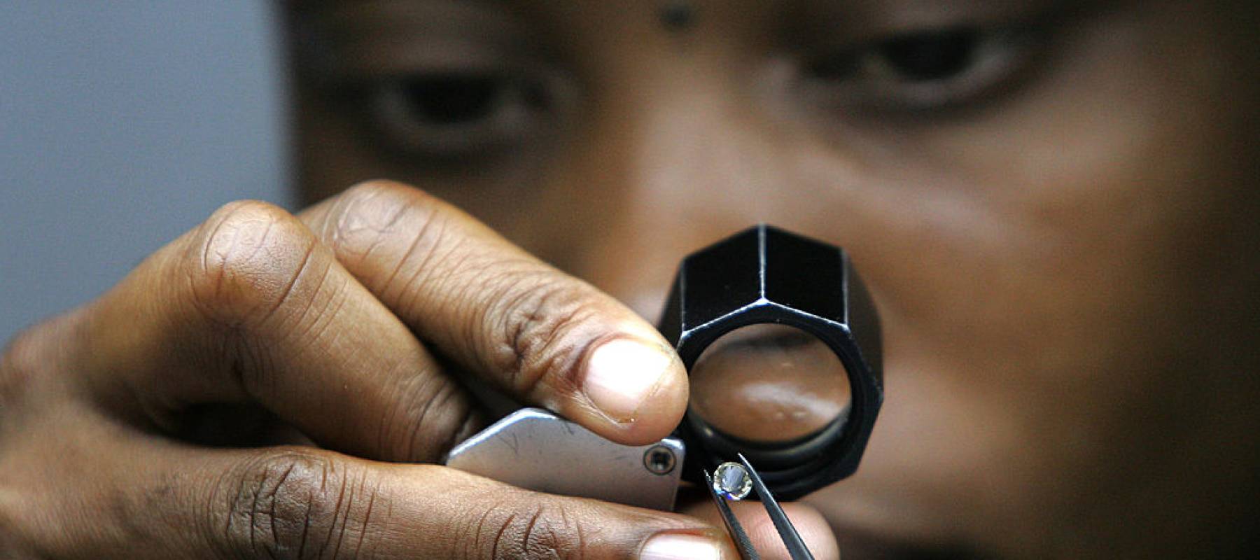 A diamond cutter looks at a stone through a jewelers loupe.