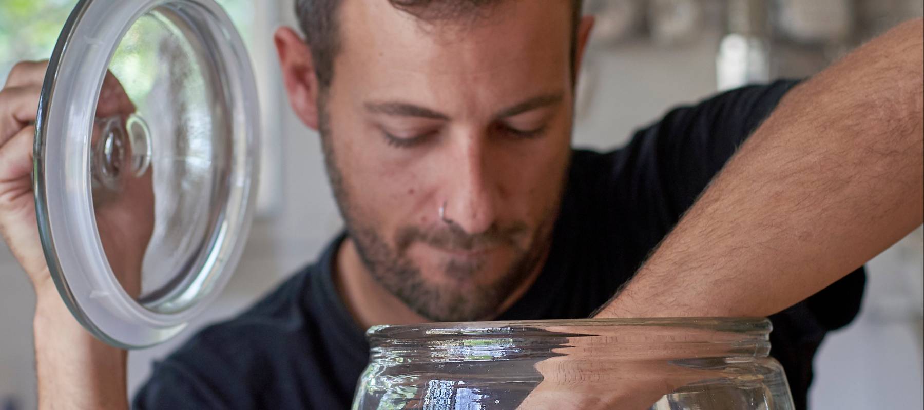 Man sitting in kitchen, looking in cookie jar, taking cookie.