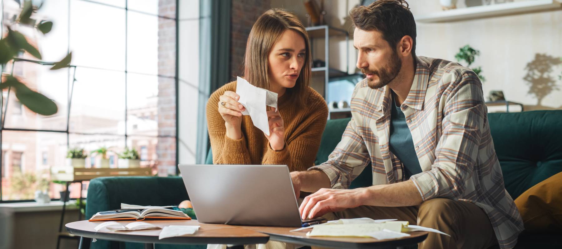 Man and woman sitting in front of a computer and talking, as woman holds and points to a piece of paper.