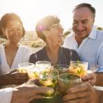 Senior multiracial friends cheering with alcohol free mojitos on the beach at sunset - Mature people having fun during summer vacation - Focus on right people faces