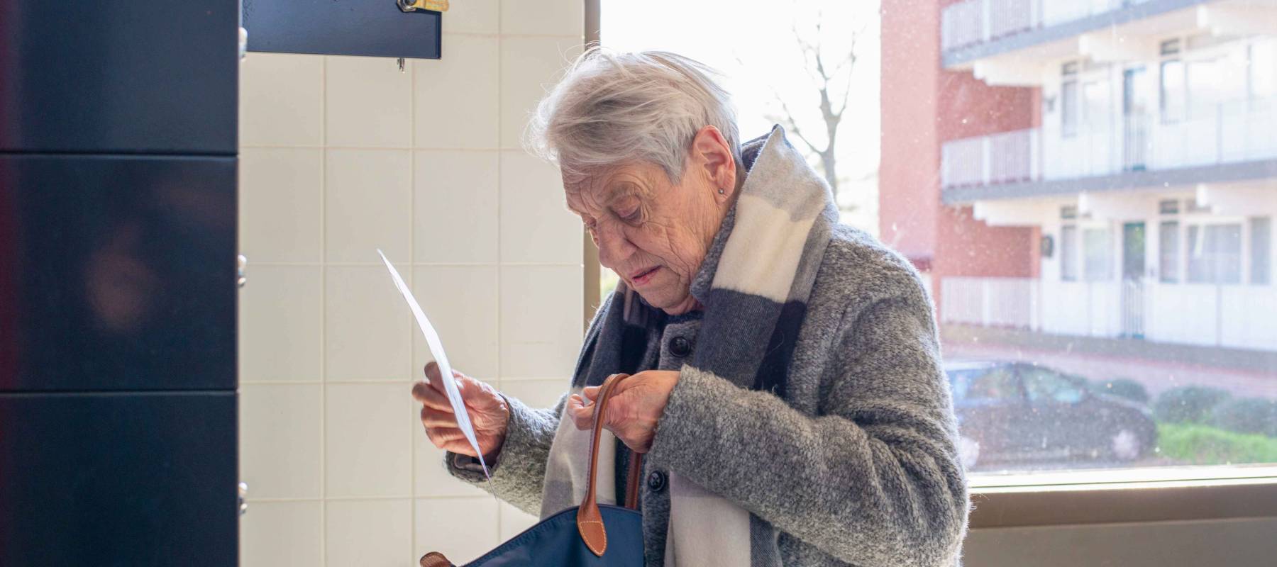 Elderly woman checking her mail by the window light.