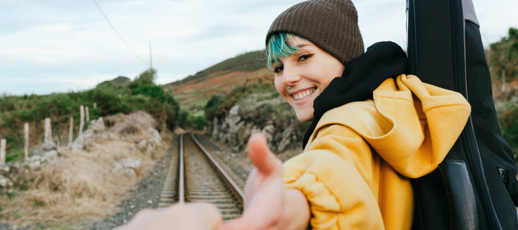 Woman wearing hat reaches out hand to the camera, leading forward.