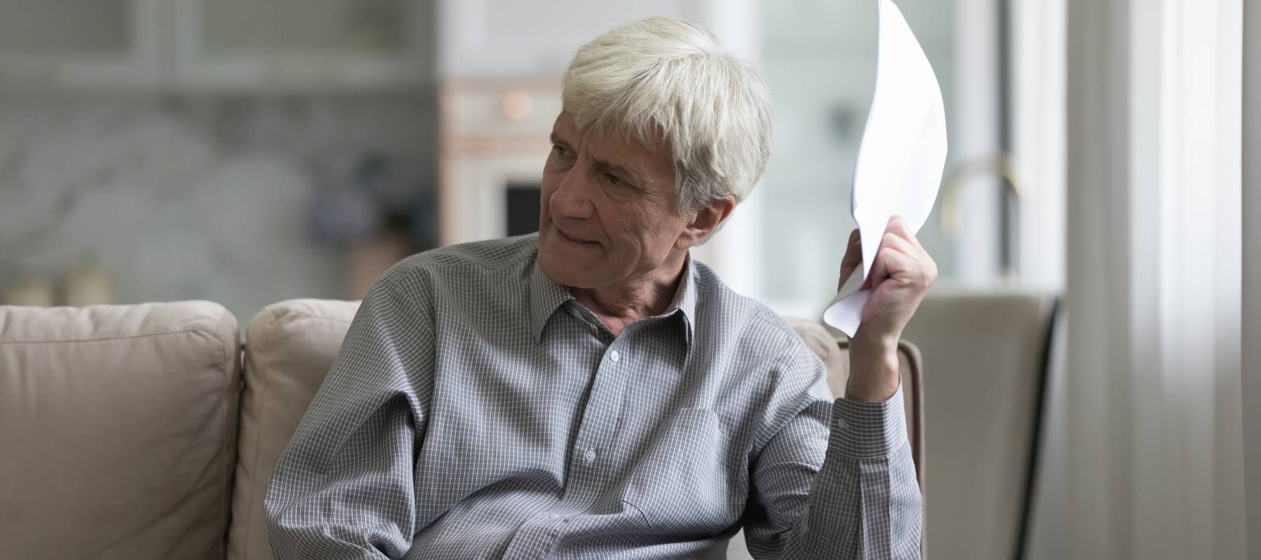 Elderly gentleman with white hair holding a piece of paper angrily in his hand.