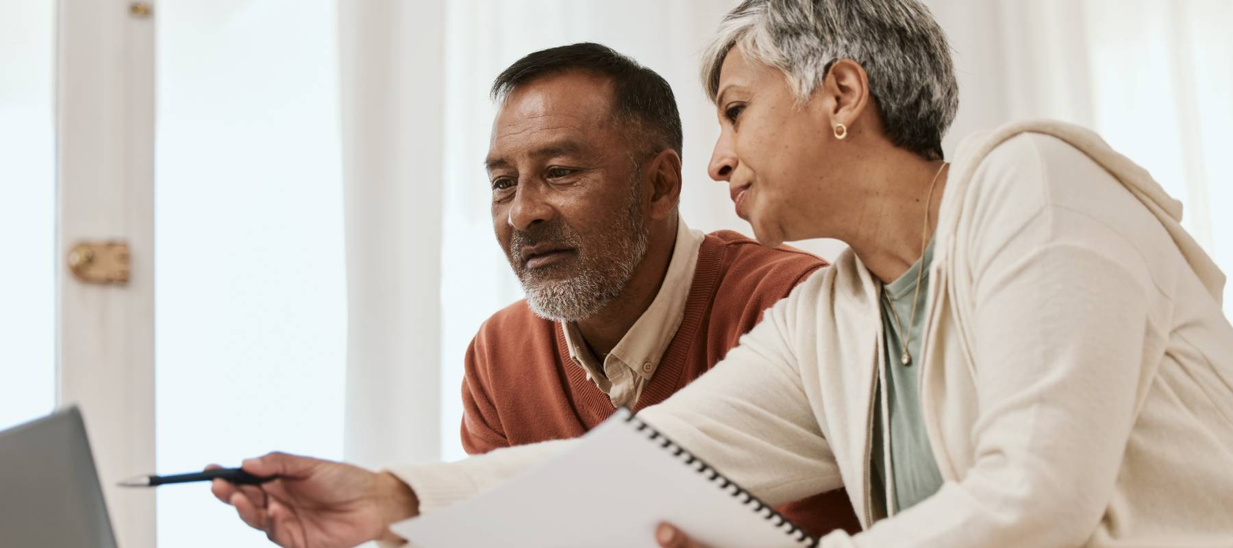 A mature couple sitting on a couch in front of a laptop and analyzing something on the screen.