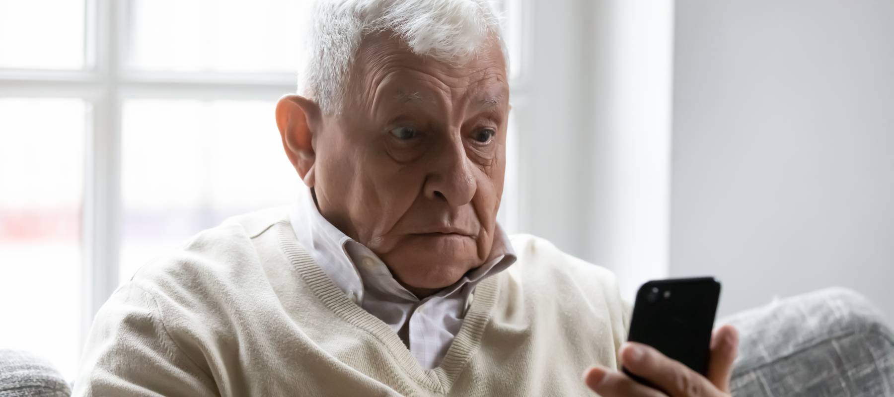 Shocked elderly man with white hair stares at his smartphone.