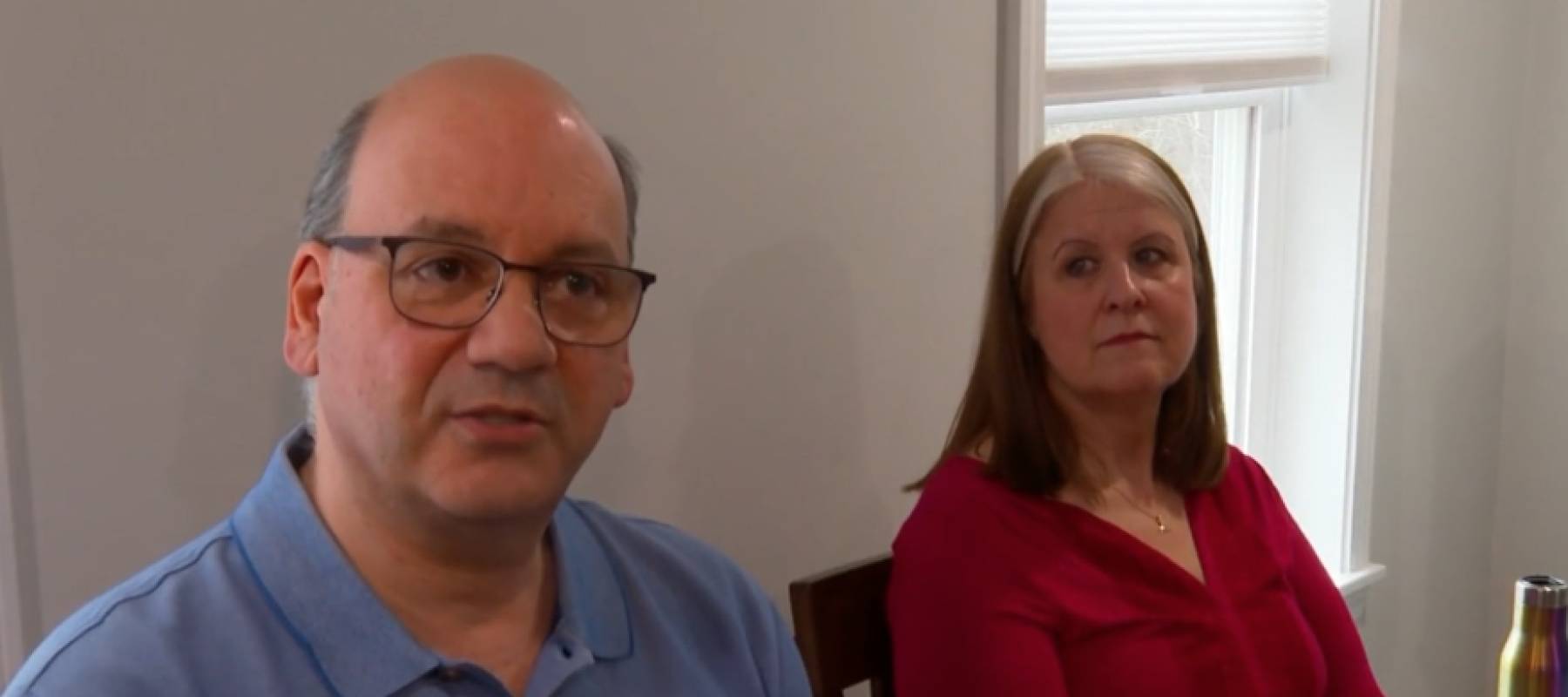 Couple sitting at dining room table, looking at camera, upset.
