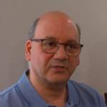 Couple sitting at dining room table, looking at camera, upset.