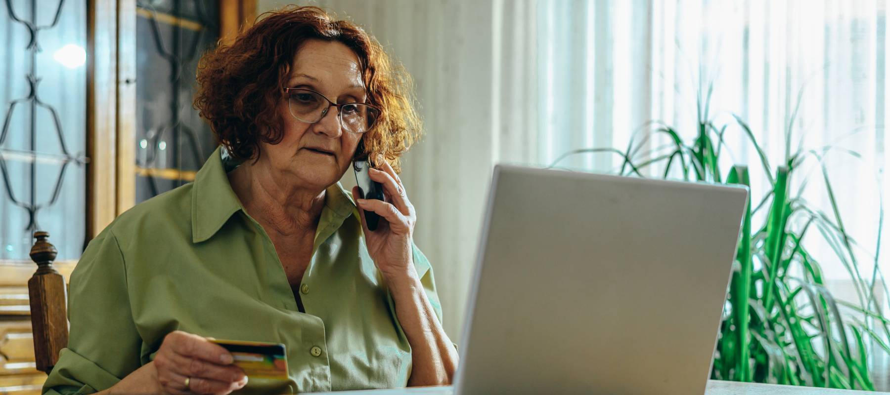 Senior woman using a laptop and a smartphone at her dining room table.