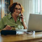 Senior woman using a laptop and a smartphone at her dining room table.