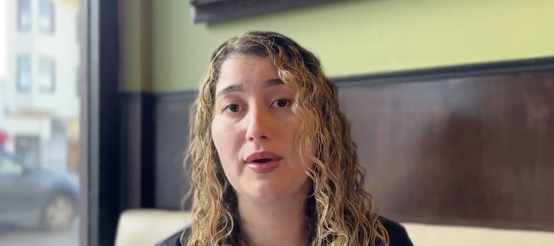 Woman sitting in restaurant, speaking directly to camera.