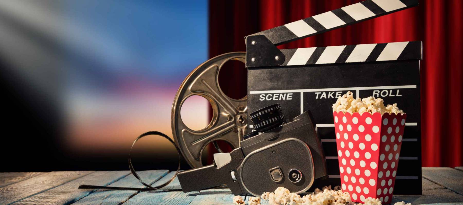 Retro film production accessories placed on wooden planks. Concept of film-making. Red curtain and movie screen on background