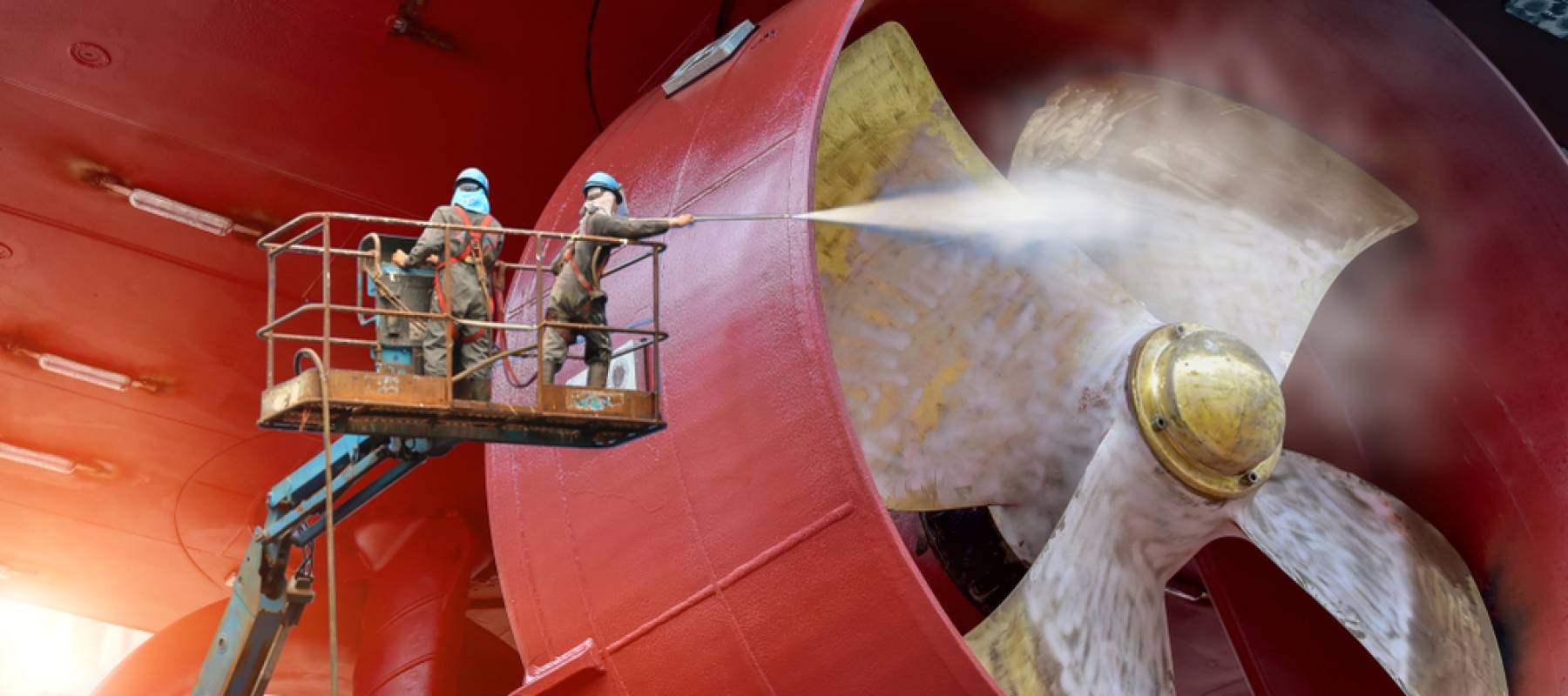 Worker on cherry picker car with safety harness in dry dock ship cleaning by water jet cleaners